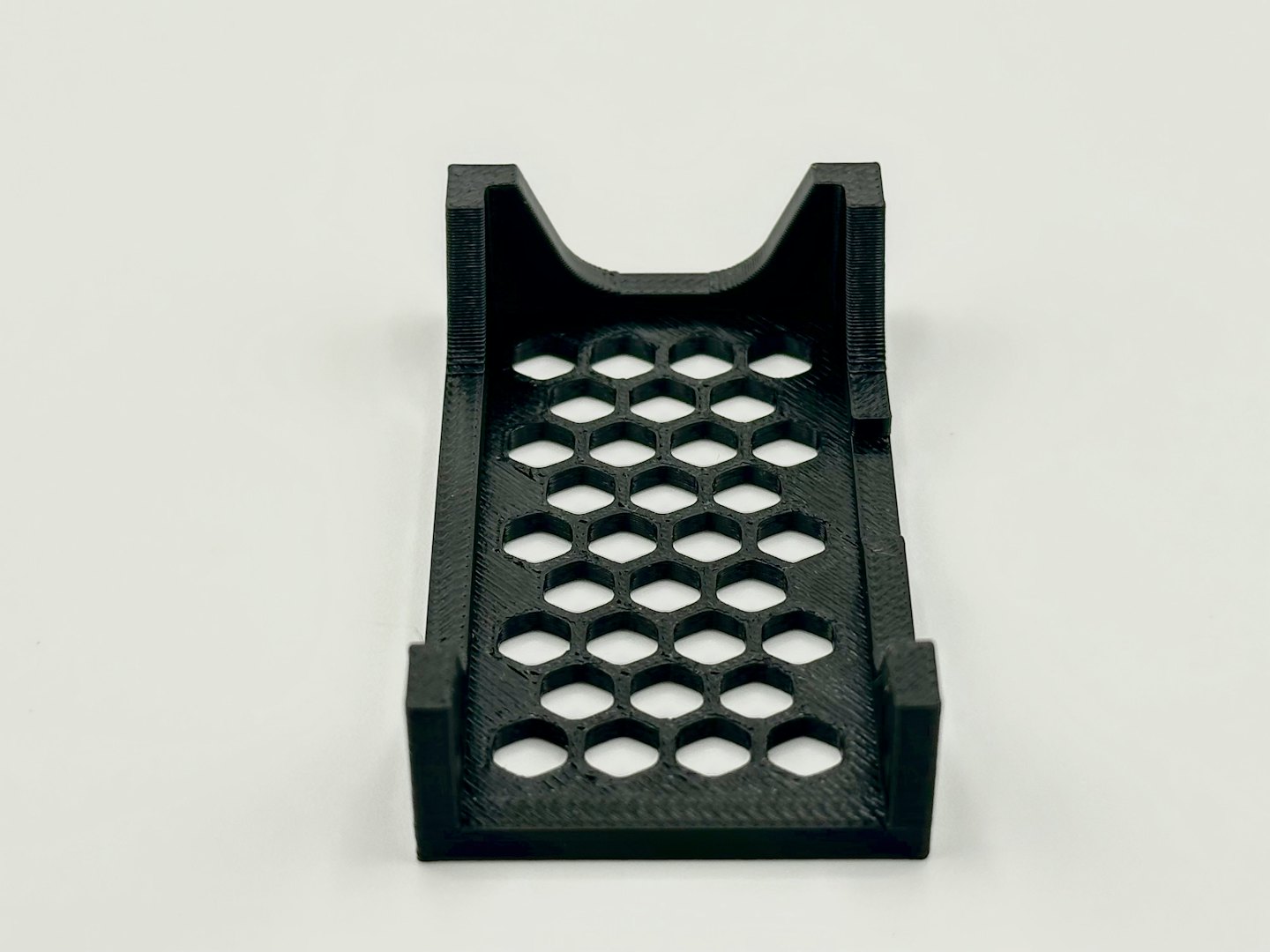 Black 3D printed object with honeycomb pattern on white background.
