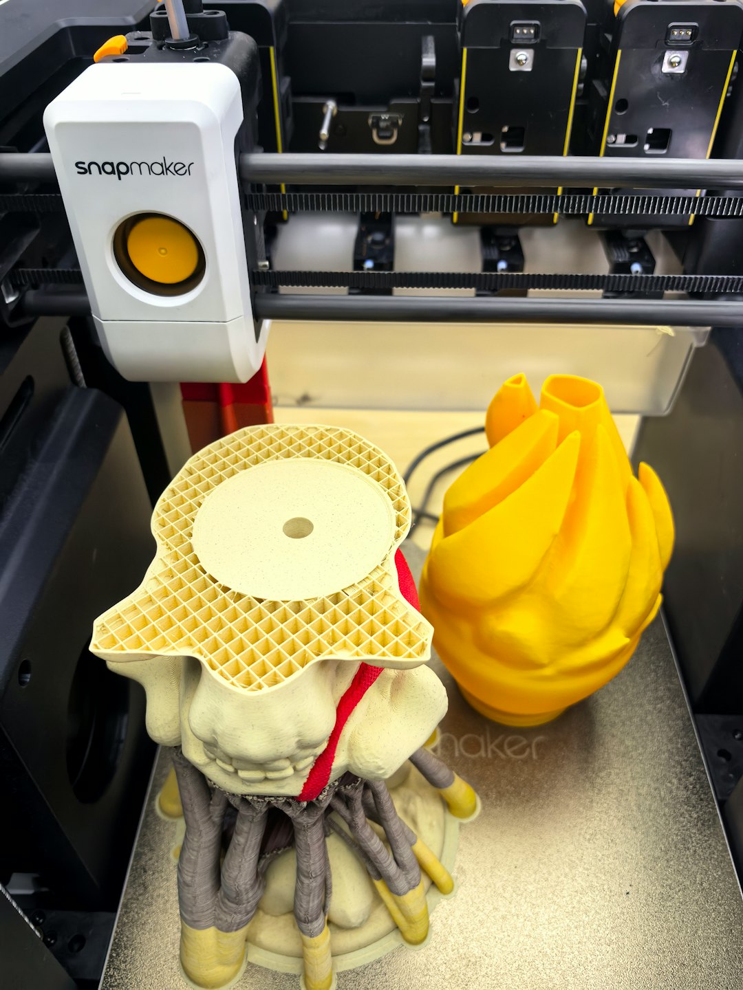 3D printer creating intricate beige and gray creature and yellow abstract sculpture.