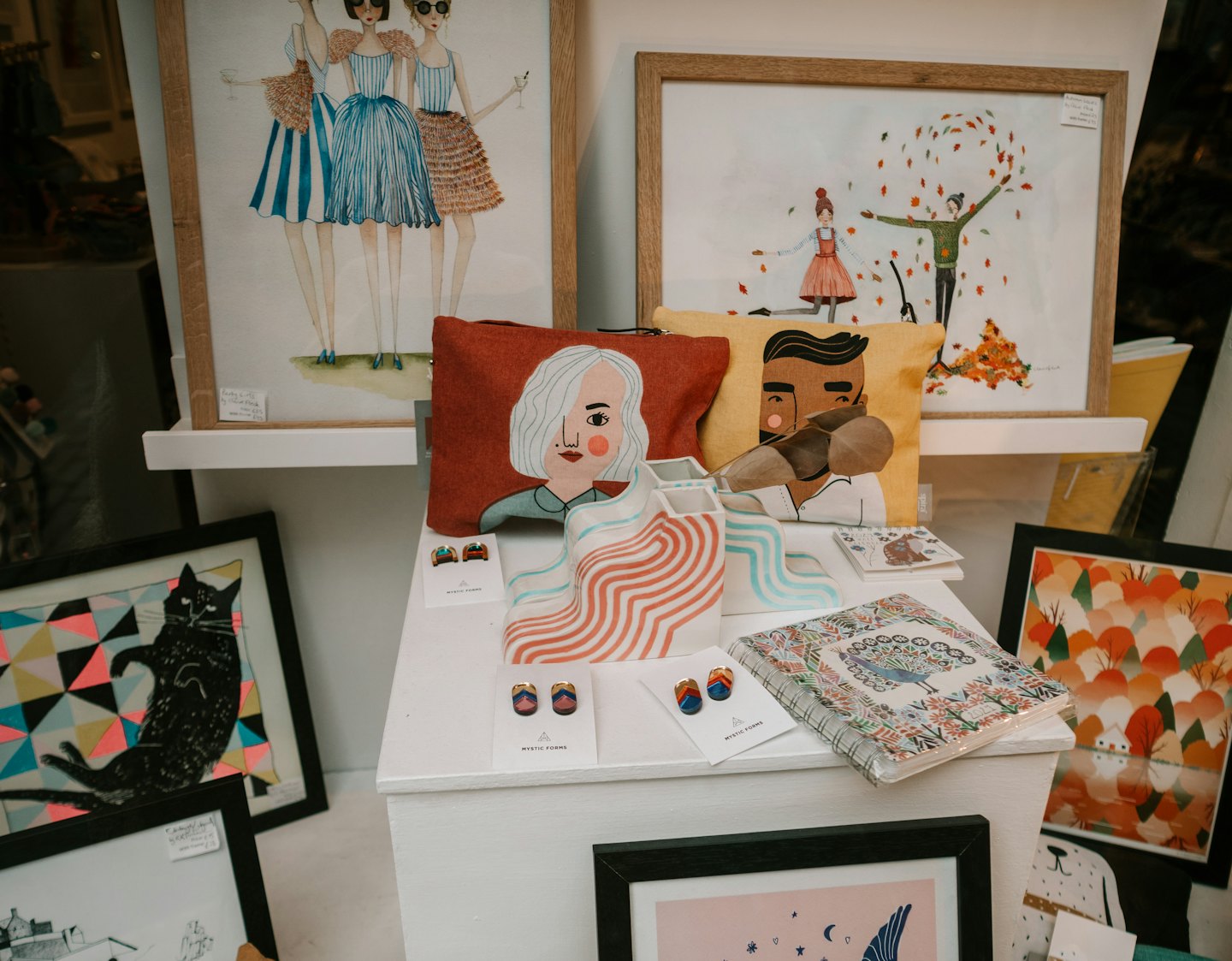 Retail shelves displaying illustrated artwork, decorative cushions, and small earrings.
